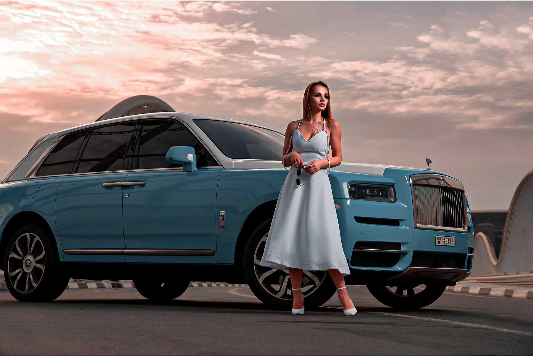 A woman in a white dress posing next to a blue Rolls Royce for a luxury car photoshoot in Dubai.