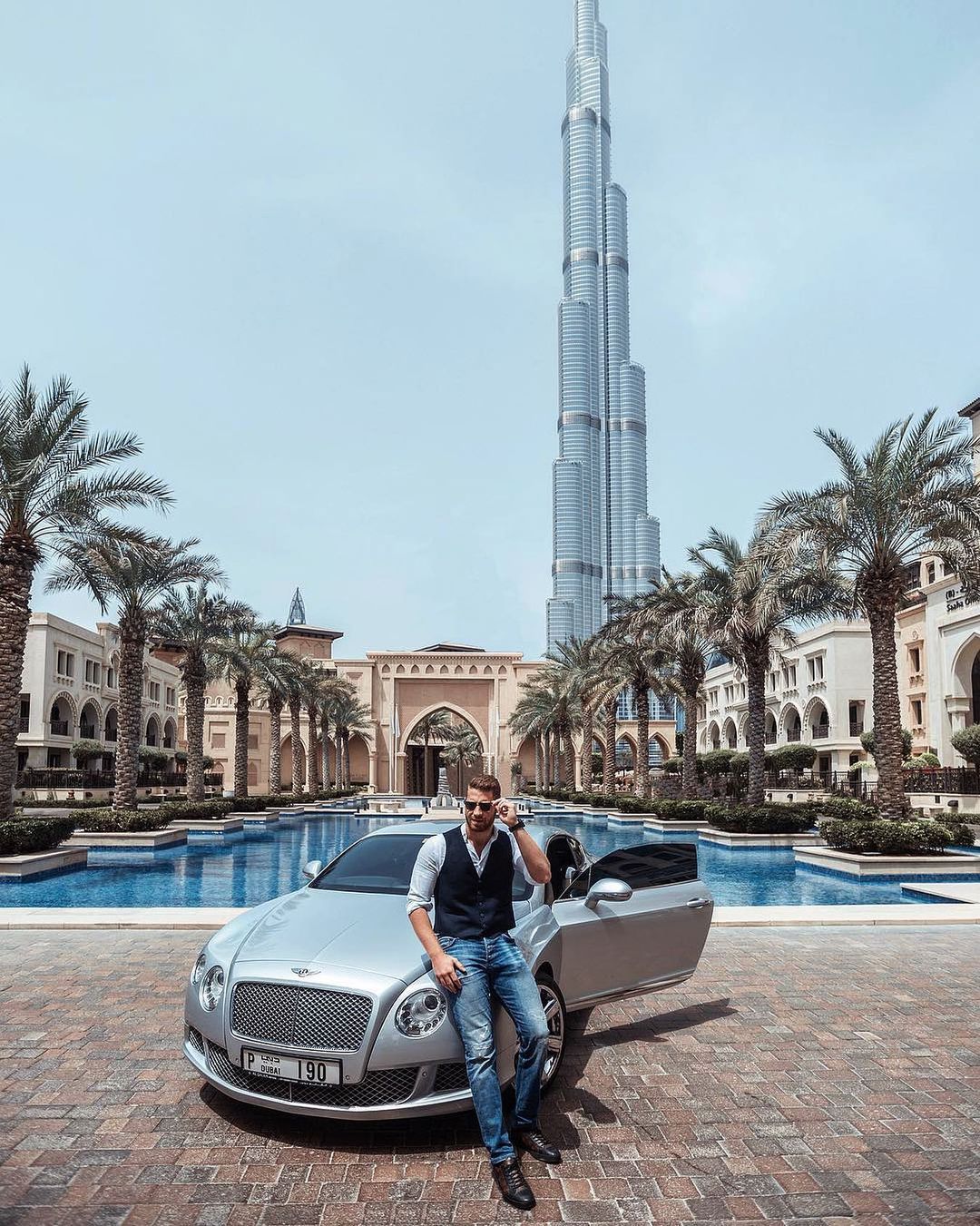 A man posing with a luxury car in front of the Burj Khalifa during a photoshoot in Dubai.